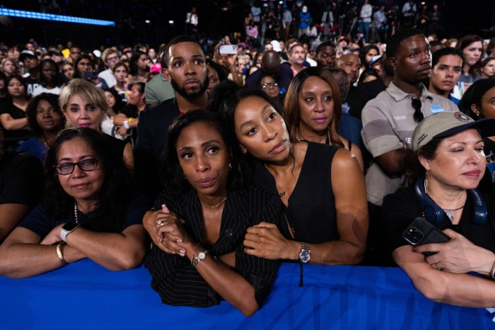 An audience listening with rapt attention, many of them young women and people of colour. Two women at the front hug each other in what looks like a gesture of hope or fear