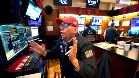 A trader wearing a red Trump hat, gestures animatedly while working at a computer