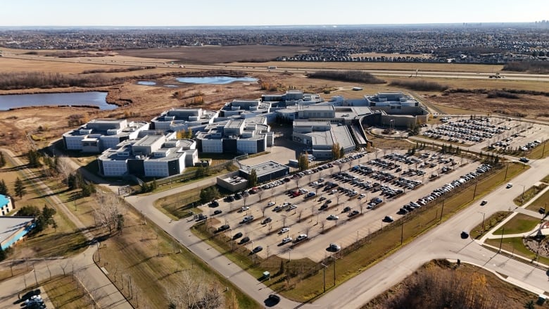 An aerial view of the Edmonton Remand Centre during the fall, showing a large complex of connected buildings and a parking lot in front of them.