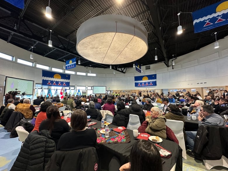 A group of over 200 people sit in a large cultural centre 