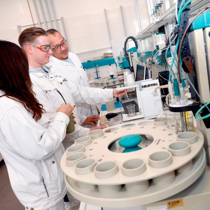 Three people in lab coats operate complex machinery