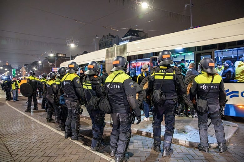 A row of officers stand in a line in front of a transit bus.