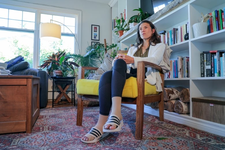 A woman is sitting in a yellow chair with her hands folded over her knee and her legs crossed.