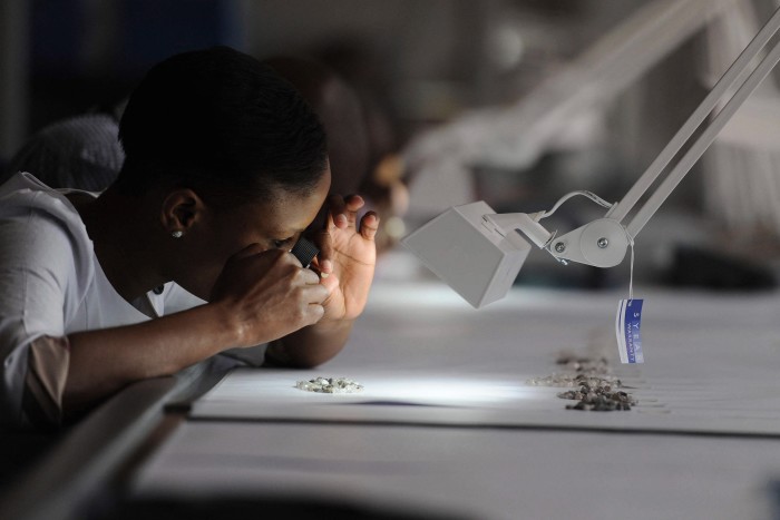 A De Beers clerk closely examines diamonds with a magnifying tool under a bright lamp