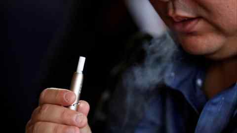 A man holds Philip Morris's Iqos 3 device, with smoke visible, during its launch event in Tokyo, Japan, on October 23, 2018.