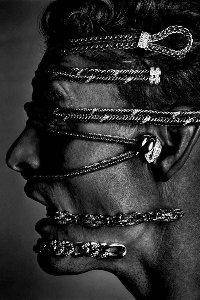 A side-on black-and-white photograph of a head wrapped in several chains of jewellery