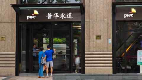 Two people enter a building with the PwC logo and the firm’s Chinese name above the entrance in Shanghai