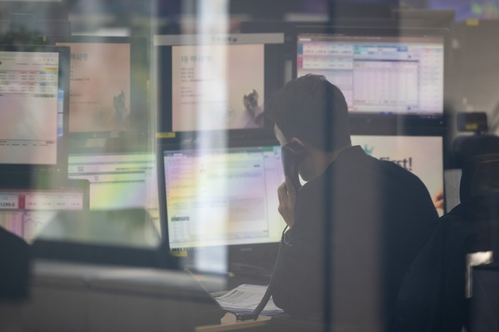 A worker in a darkened office holds a phone to his ear as he looks at a bank of computer screens