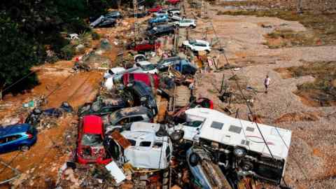 A man stands next to flooded cars piled up in Valencia, Spain