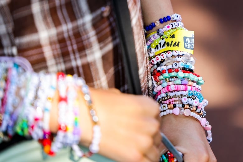 A close up image of two wrists covered with Taylor Swift bracelets is shown. 