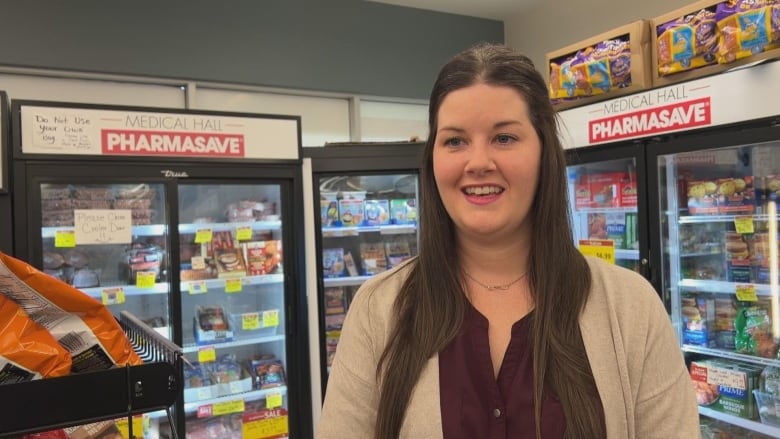 A woman with long brown hair speaks inside a pharmacy 