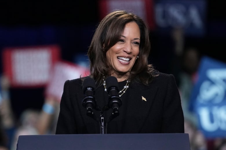 A woman in a dark suit smiles on stage during a political rally.