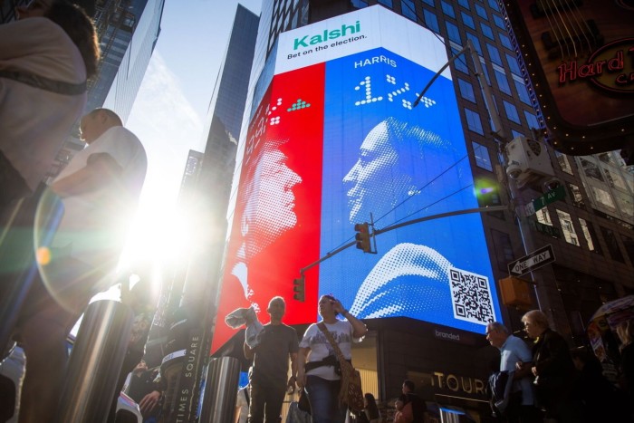 People walk by a digital billboard showing 2024 US presidential election odds across from the Nasdaq exchange in New York