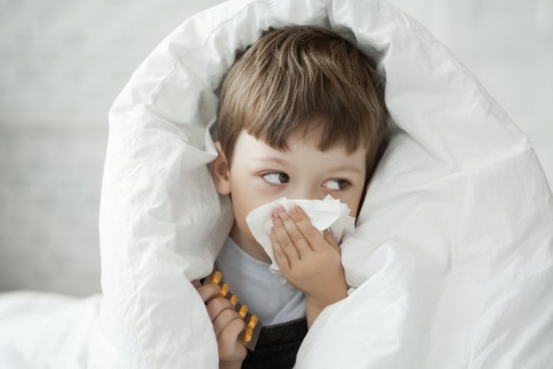 A sick child with a cold wipes his nose with a tissue.