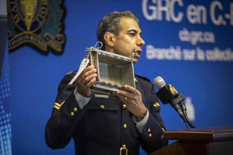 An officer in uniform holds up a square box.